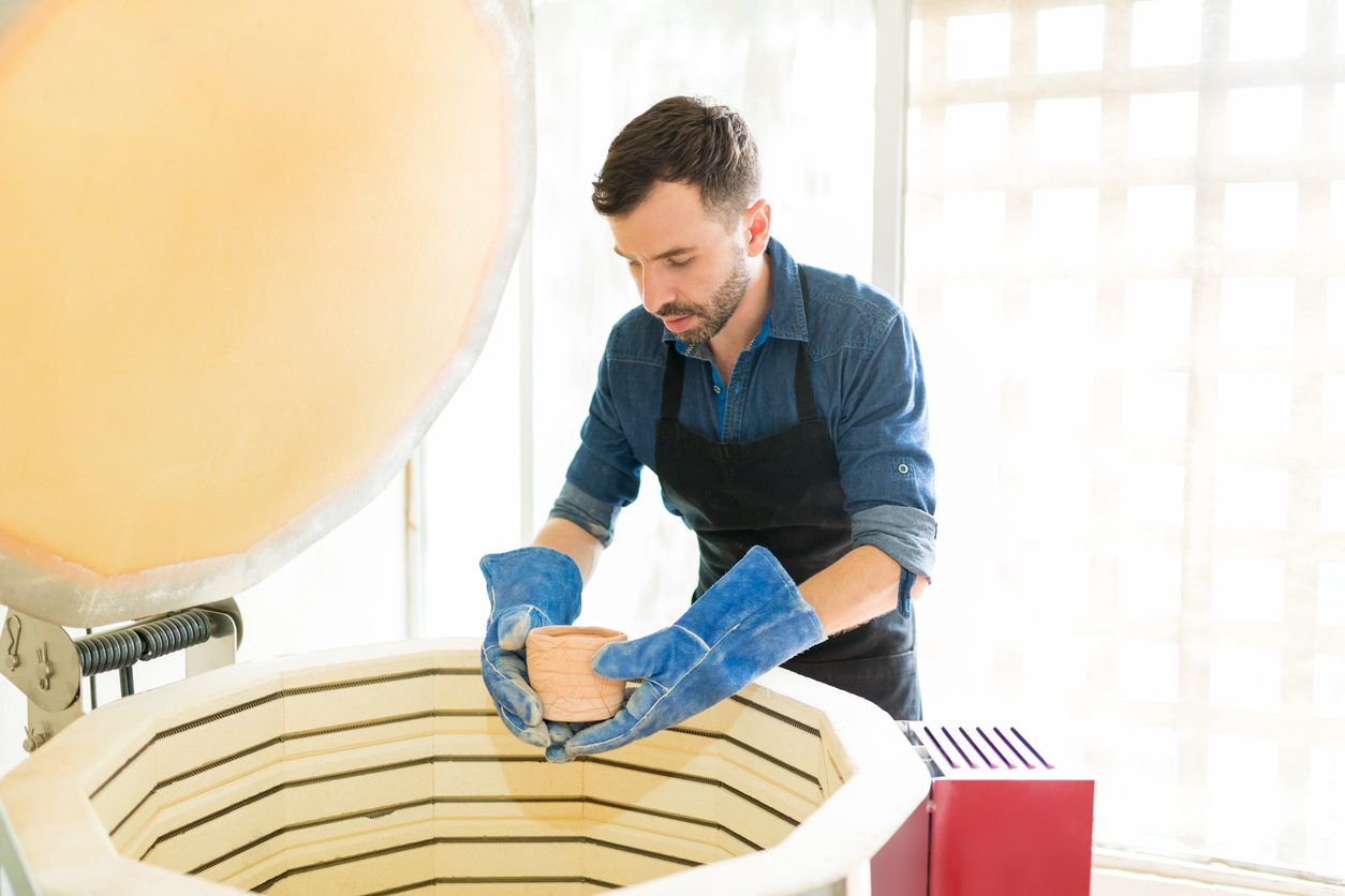 Man Placing Clay Mug Into Kiln At Pottery Studio