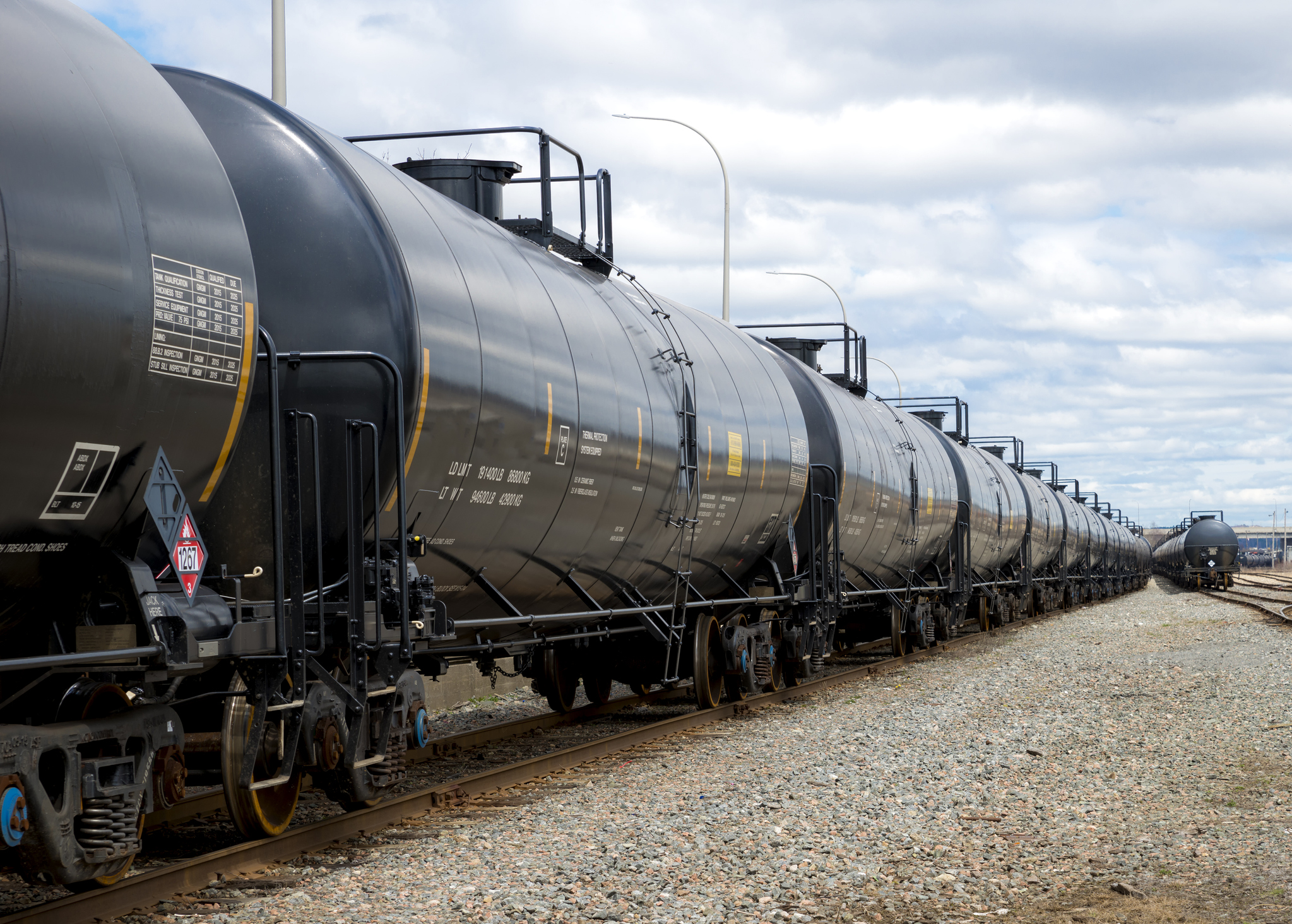 Black railway tanker cars of the type used to transport petroleum products. Several cars visible on two separate sets of tracks. Identification markings have been removed, only technical information remains.